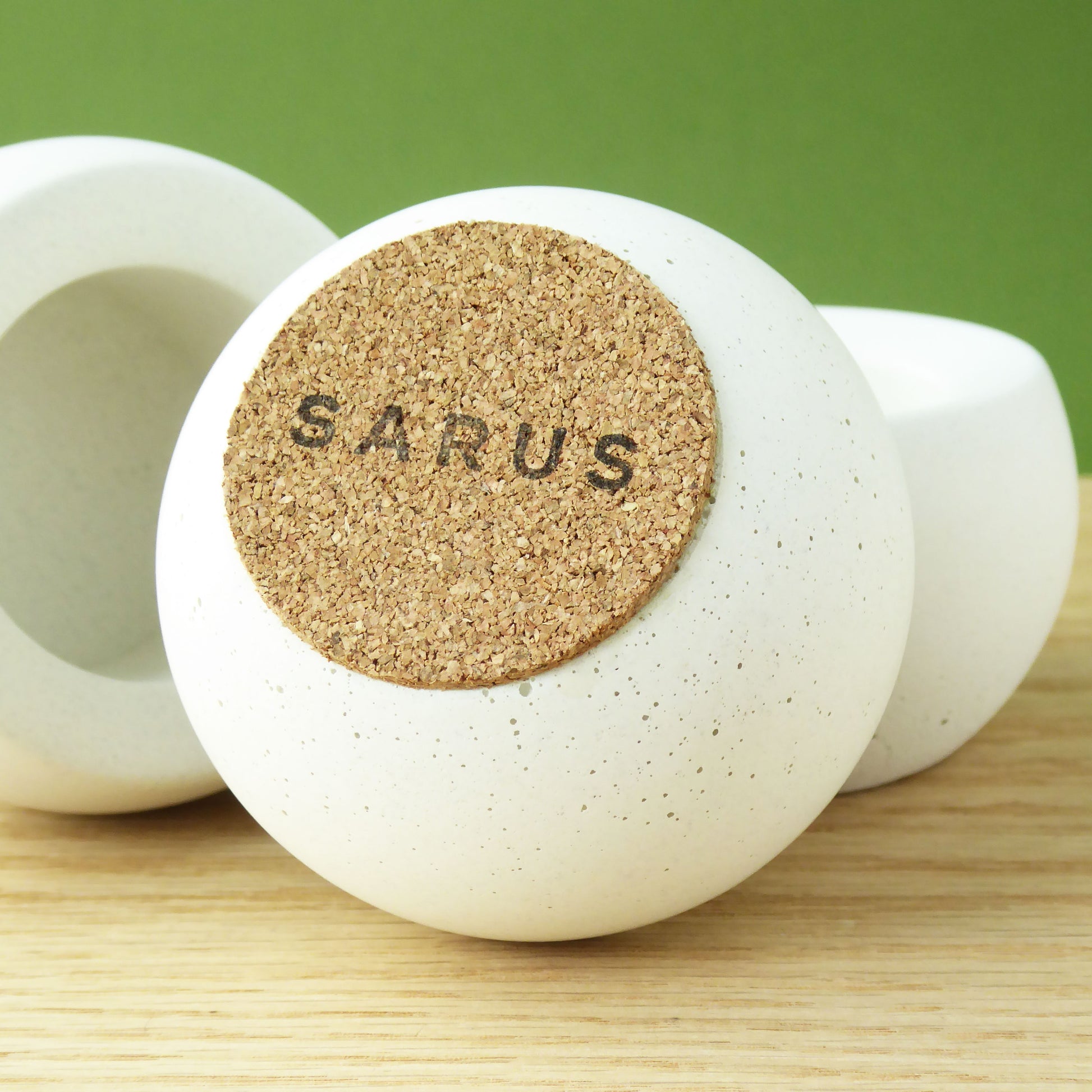 White candle holder with a cork base and SARUS logo on a wooden surface.