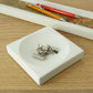 Metal stationery clips in a white concrete tray with a pen tray in the background on a wooden desk